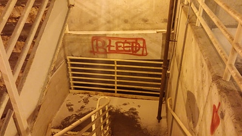 下り階段の踊り場の壁に書かれた「BLEED」の赤文字